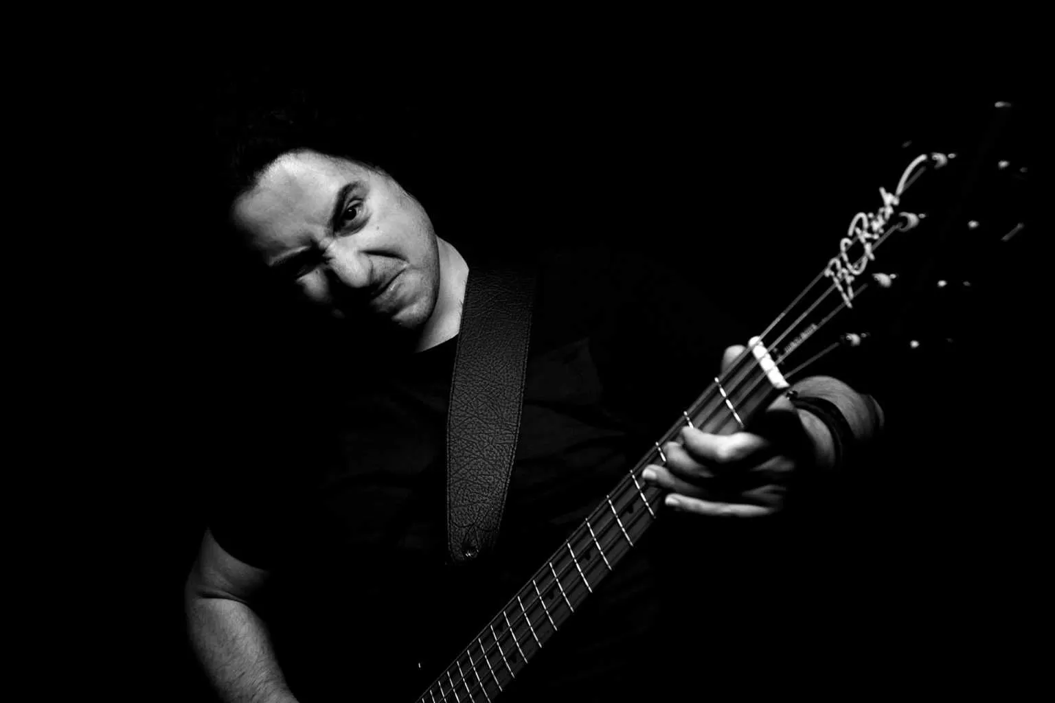 Dramatic black and white portrait of a guitarist playing an electric guitar under low-key lighting against a dark background.