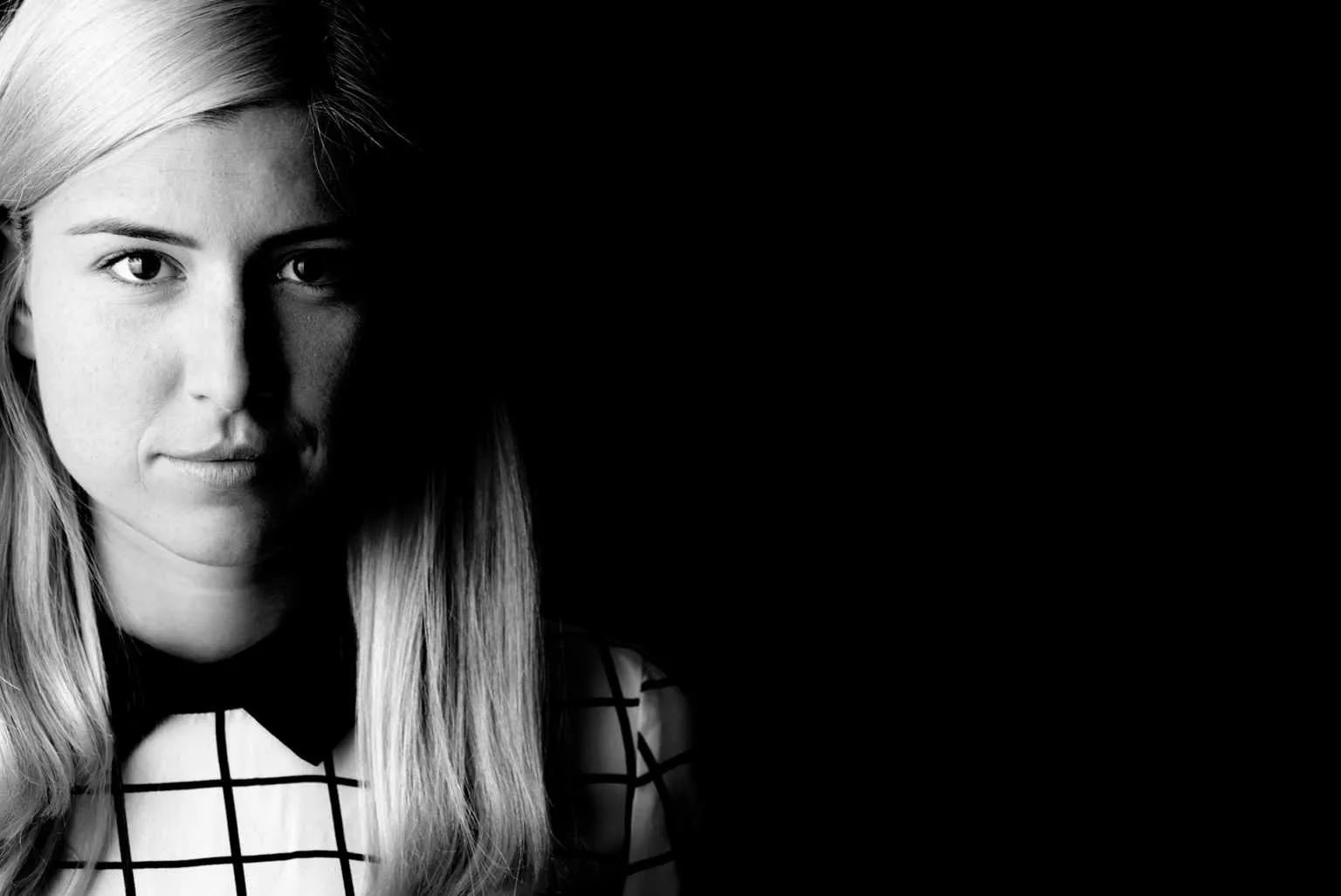 Black and white half face portrait of a blonde woman with strong shadow and clean graphic background