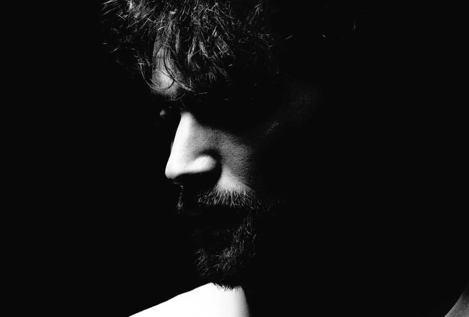 High contrast black and white side profile of a bearded man with face fading into shadow