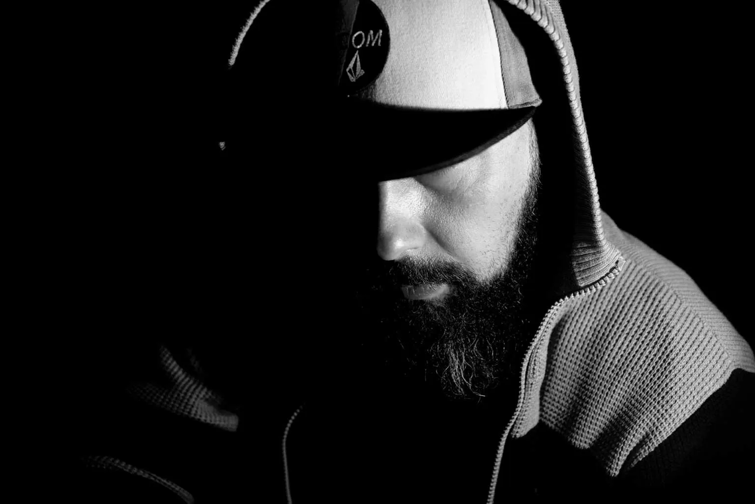 Low key portrait of a bearded man wearing a cap with face partially hidden in shadow