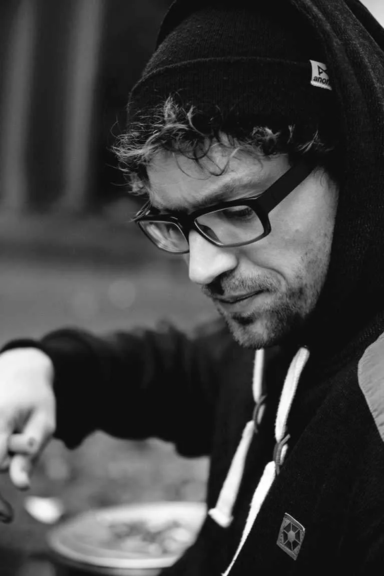 Black and white candid portrait of a man wearing glasses and a beanie, looking down.