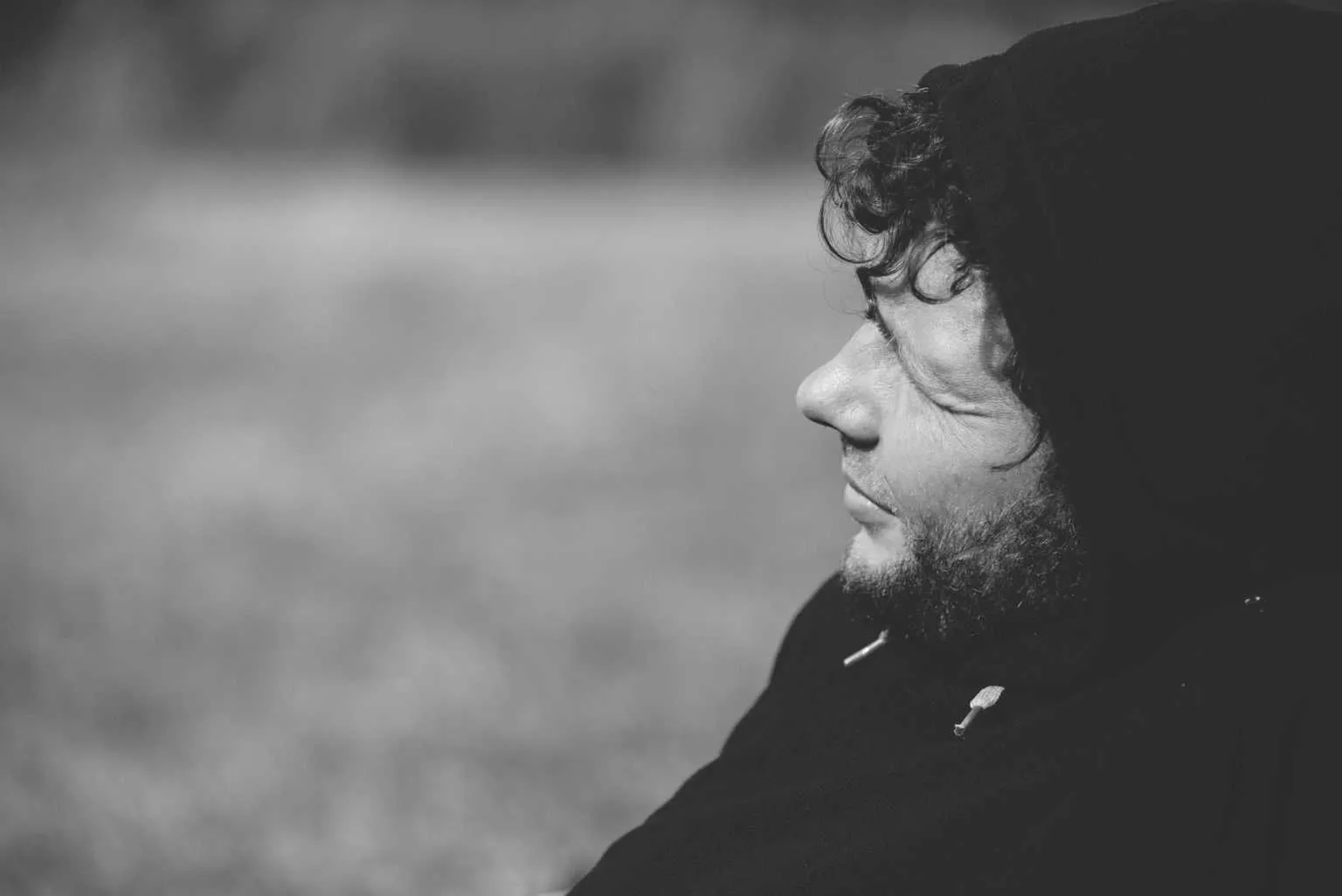 Black and white side profile portrait of a man wearing a hooded sweatshirt looking into the distance outdoors.