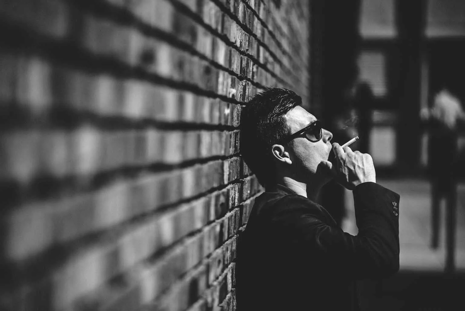 Portrait with natural light of a young man leaning against a brick wall smoking a cigarette