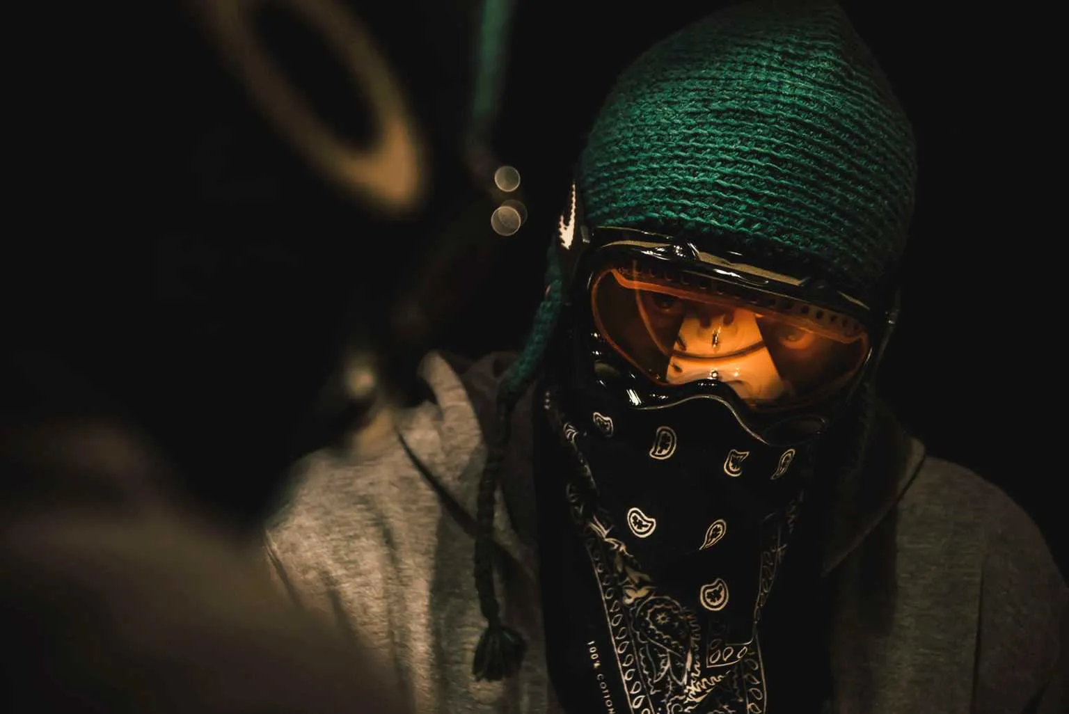 Cinematic portrait of a person wearing ski goggles, a knit beanie, and a bandana covering the face in dramatic night lighting.