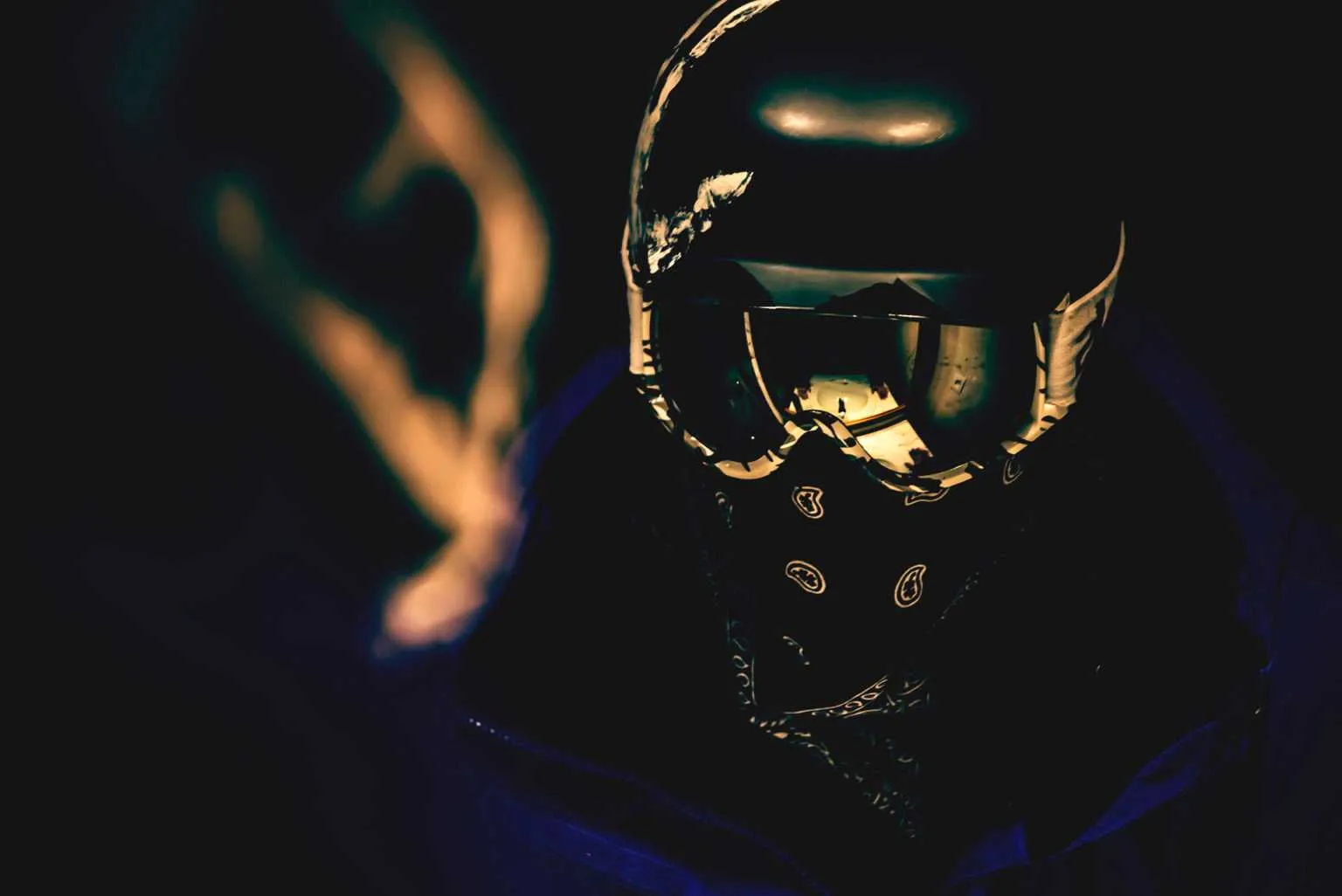 Dark cinematic portrait of a person wearing a reflective snowboard helmet and bandana with neon light reflections.