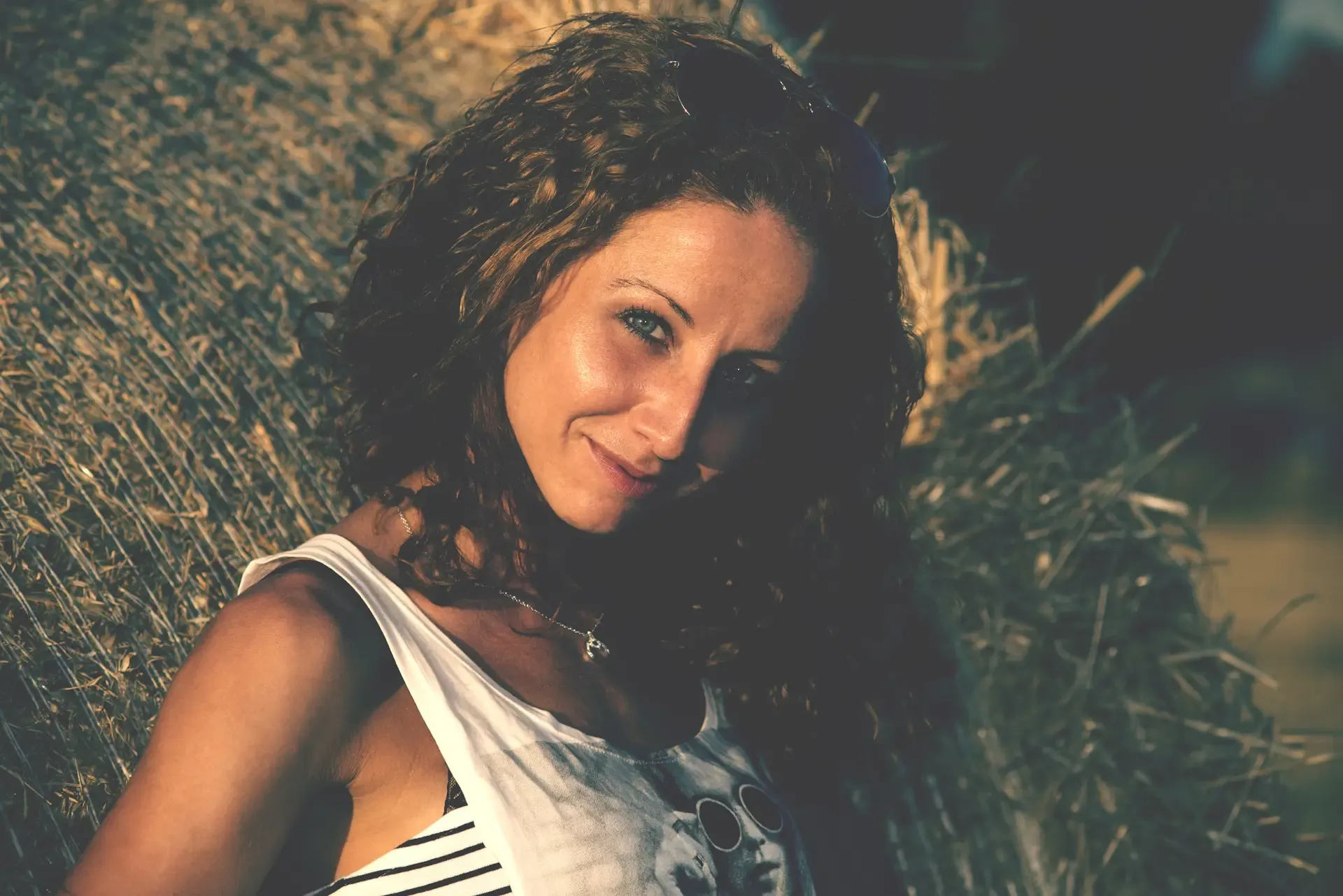 Natural outdoor portrait of a woman with long curly hair, wearing a white top.