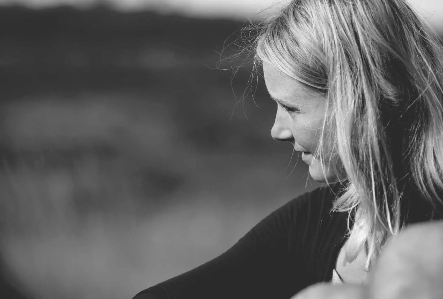 Black and white side profile portrait of a woman with blonde hair looking into the distance outdoors.