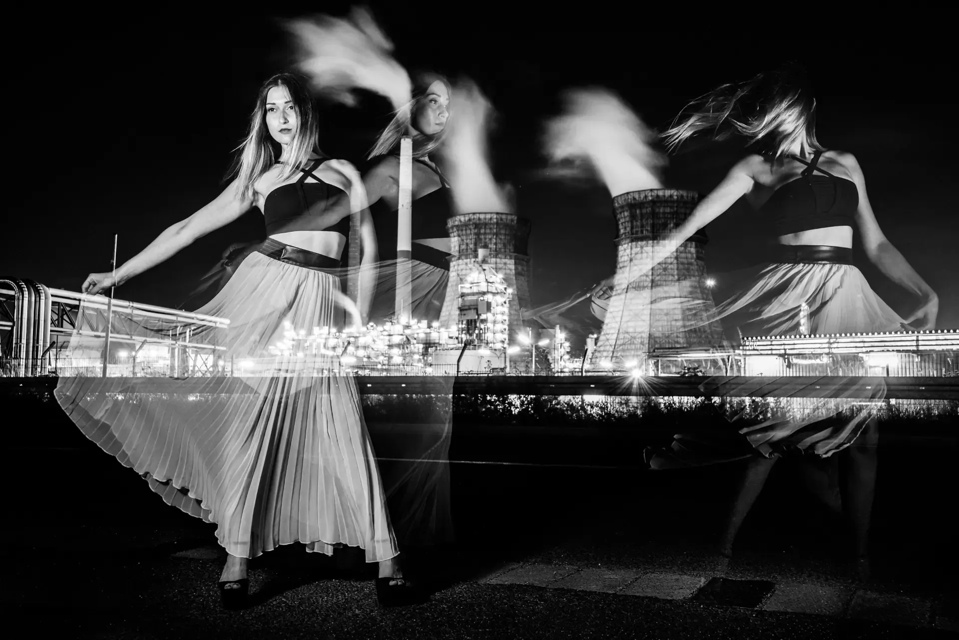 Black and white double exposure of a woman dancing with layered silhouettes blended with a brightly lit industrial power plant at night.