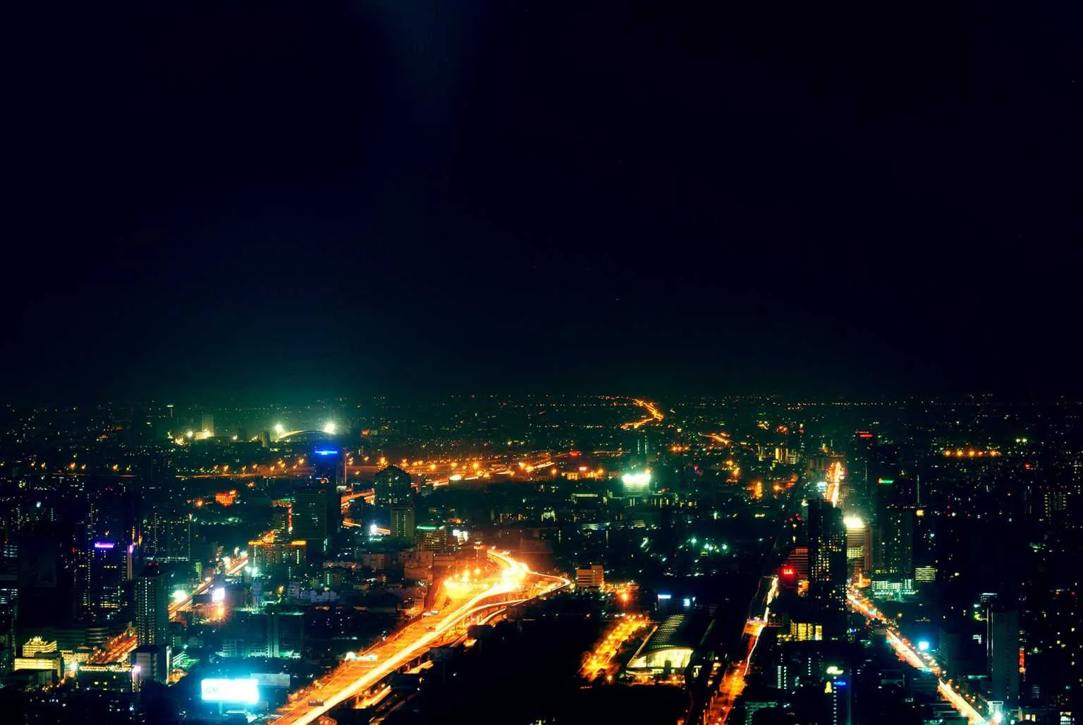 Aerial night view of a large city with glowing highways and illuminated buildings stretching across the skyline.