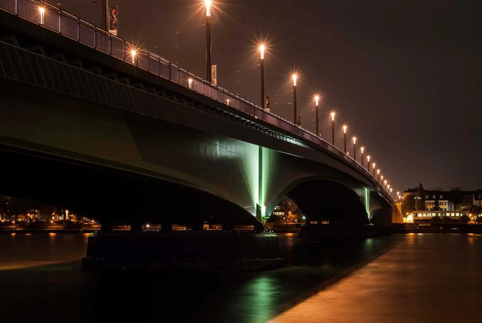 Modern bridge illuminated by streetlights at night with reflections in the river below.