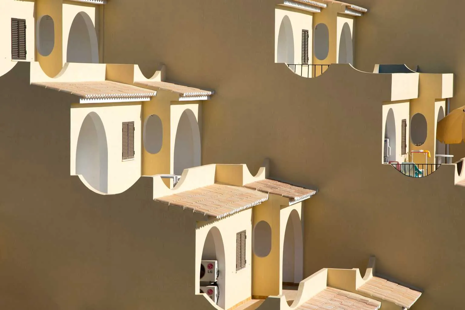 Geometric pattern of Mediterranean-style balconies and arches on a warm beige building facade.