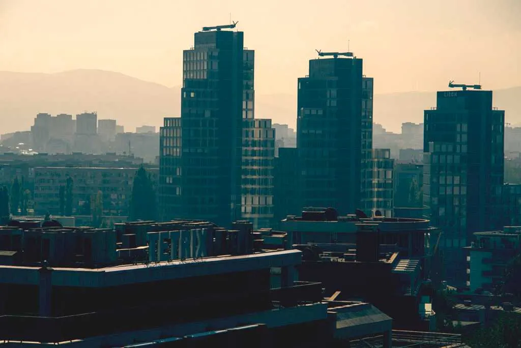 Cluster of modern high-rise residential towers rising above an urban neighborhood with mountains in the background.