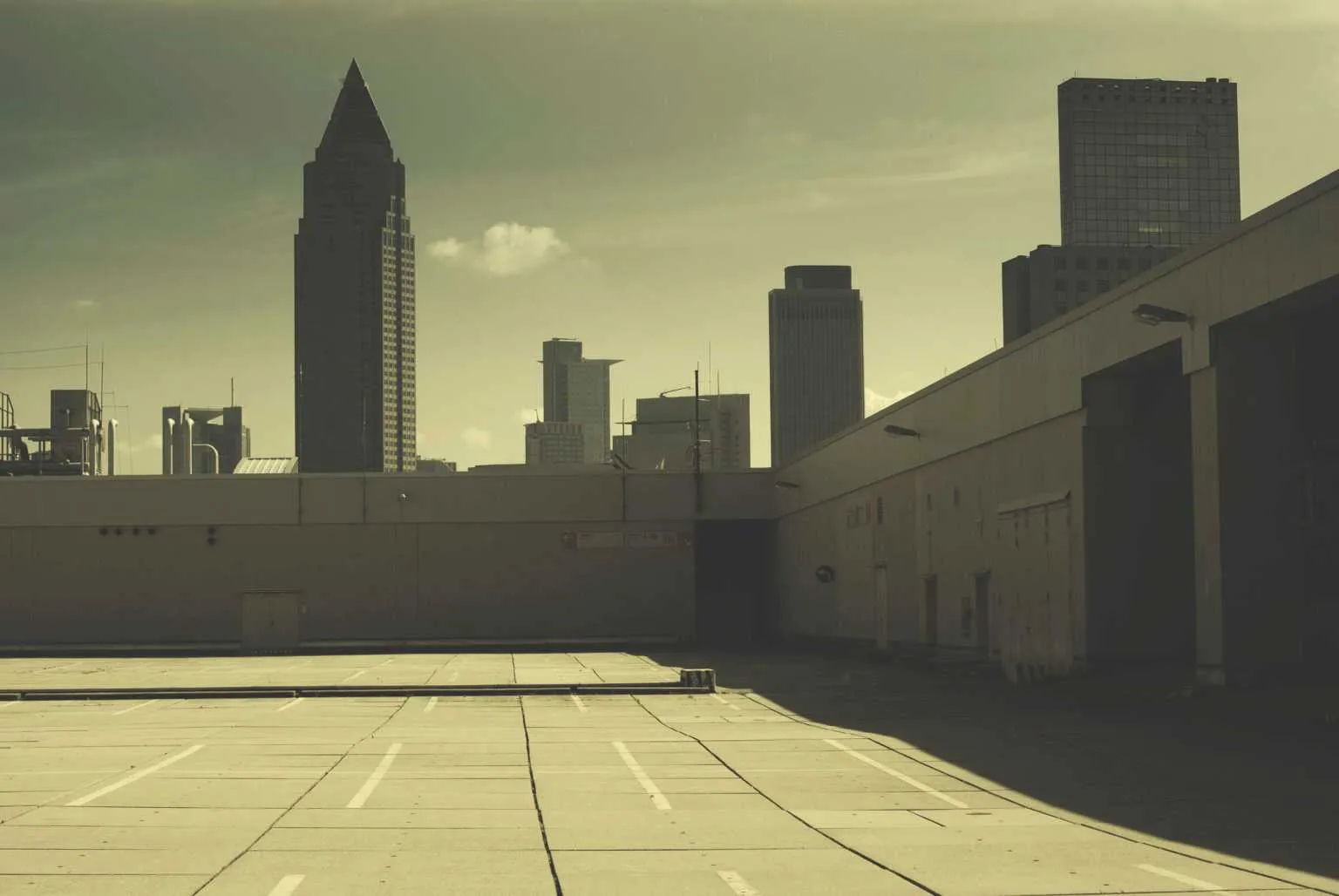 Empty rooftop parking lot with city skyline silhouettes in the distance under warm evening light.
