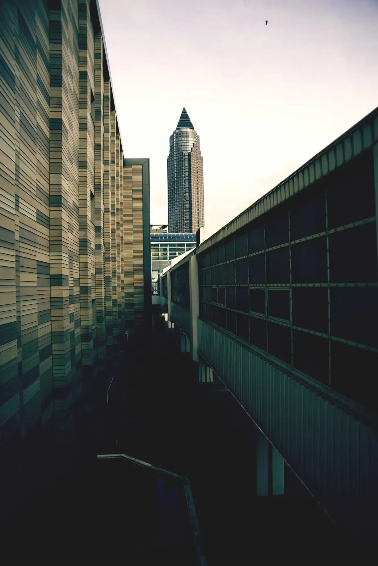 A tall modern skyscraper framed between two long buildings forming a narrow urban corridor.