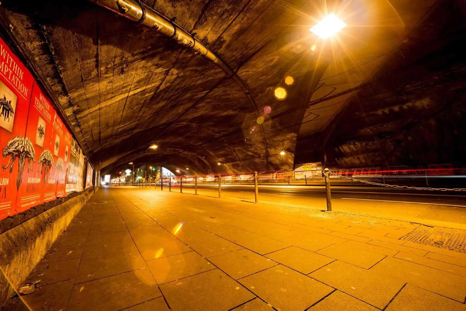 City tunnel at night with warm street lighting and long exposure light trails from passing vehicles.